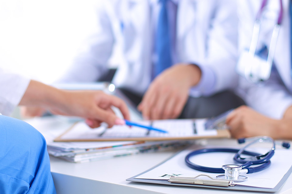 Three people's hands holding medical records as if consulting