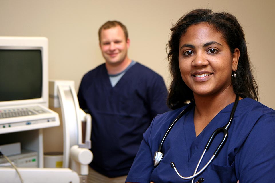 A female and a male medical professional next to computer monitor and keyboard