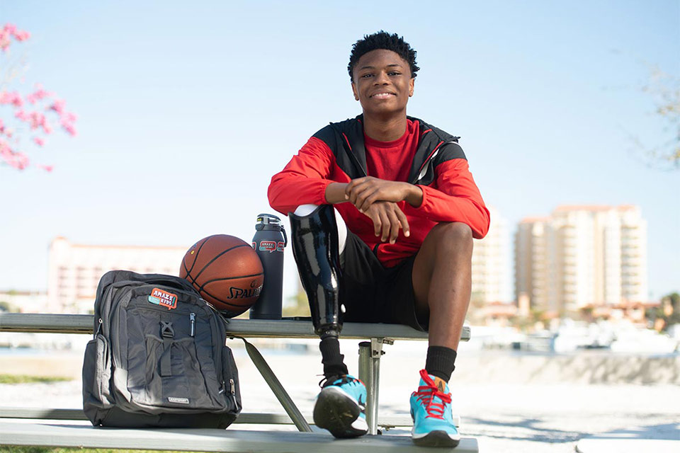 Patient avec une jambe prothétique, souriant sur un banc à côté d’un terrain de basket