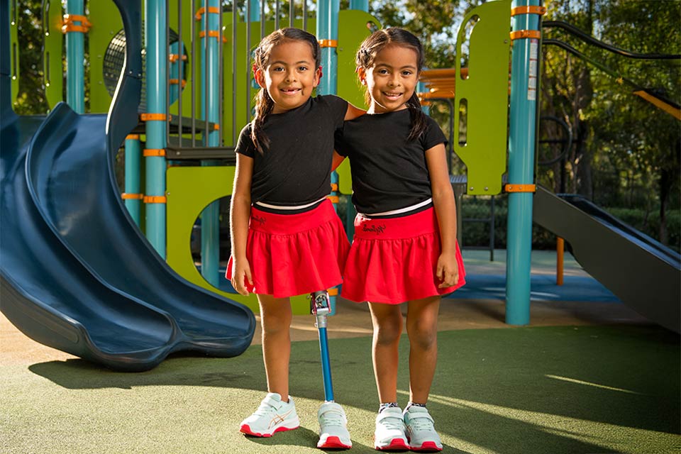 two female children on playground, one with prosthetic leg