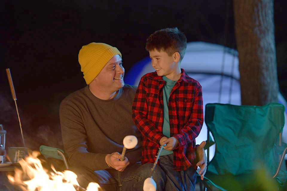 un père et son fils font rôtir des guimauves au-dessus du feu de camp