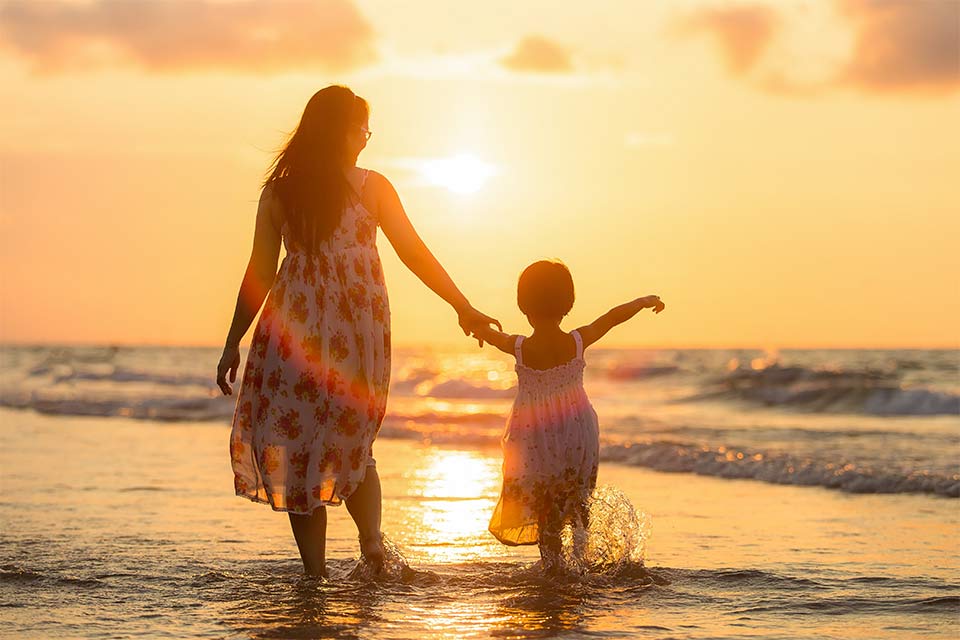 Mère et fille marchant dans l'eau à la plage au coucher du soleil