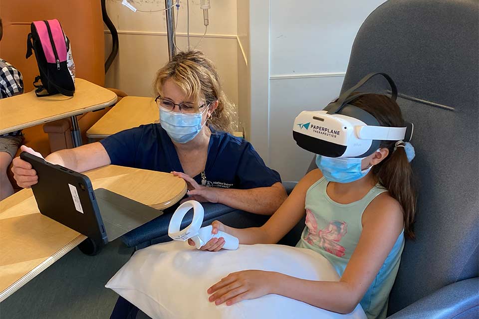 Patiente portant un casque de réalité virtuelle à côté d’une spécialiste du milieu de l’enfant