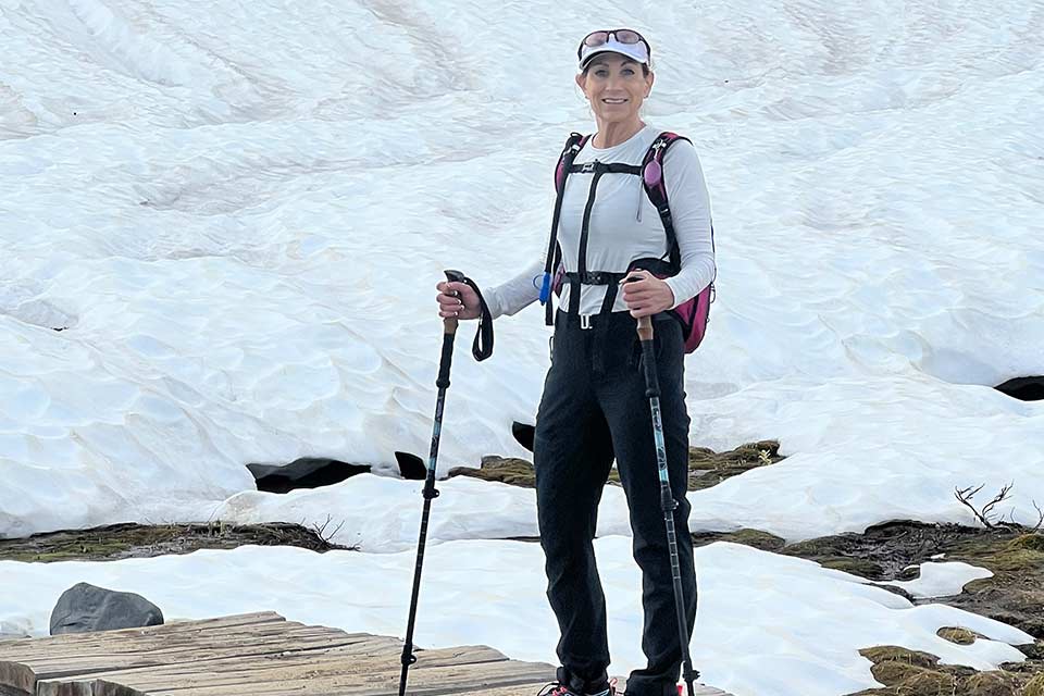 Lynda debout à côté d’une montagne couverte de neige tenant des bâtons de randonnée