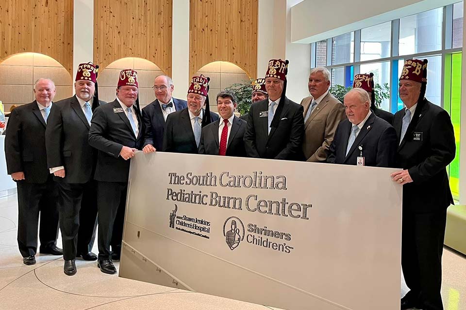 Miembros de Shriners International y líderes de MUSC parados frente a al letrero del centro de quemados de marca compartida