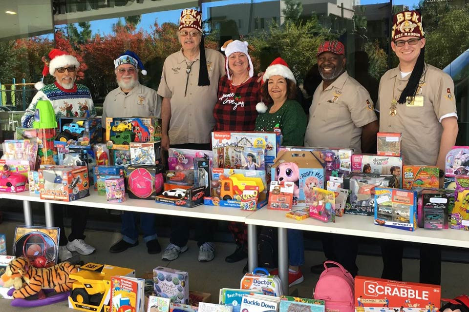 Shriners y voluntarios frente a una mesa llena de donaciones de juguetes