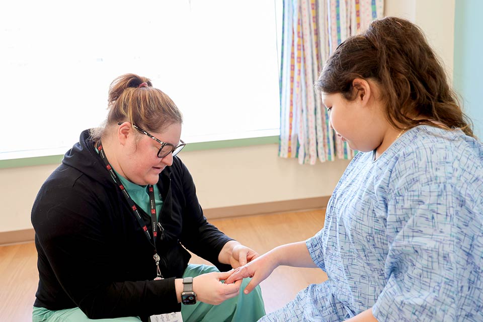 Une professionnelle de la santé soignant des brûlés examine les cicatrices de brûlure sur la main d’un patient