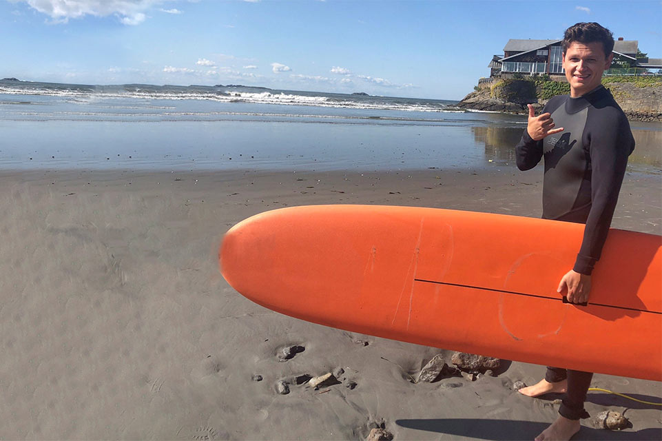 Peter, paciente con quemaduras, sosteniendo una tabla de surf en la playa