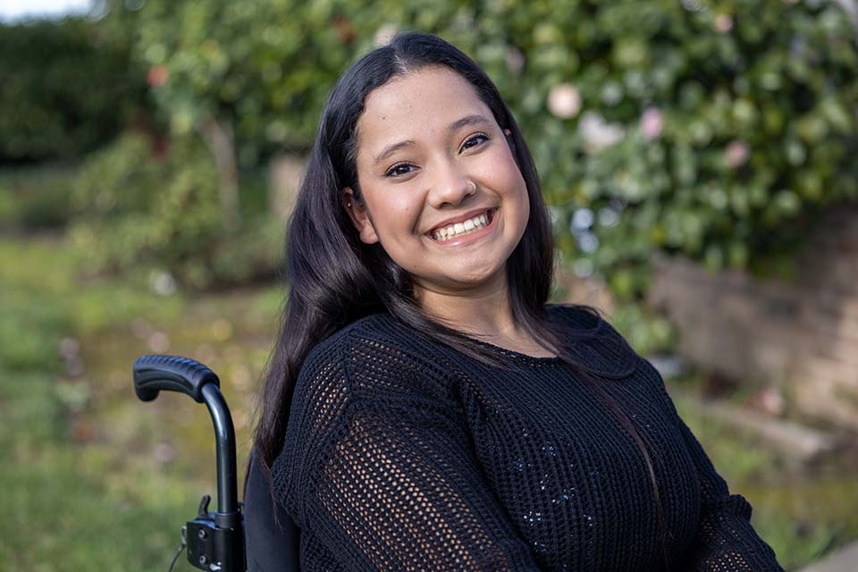 Paciente de sexo femenino con espina bífida sentada en silla de ruedas al aire libre, sonriendo