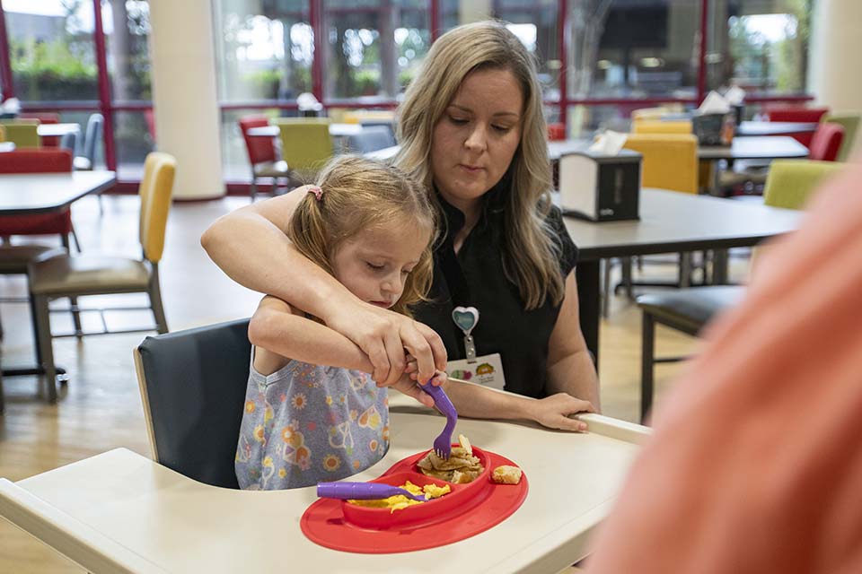 una terapeuta ayudando a una paciente a comer en la cafetería