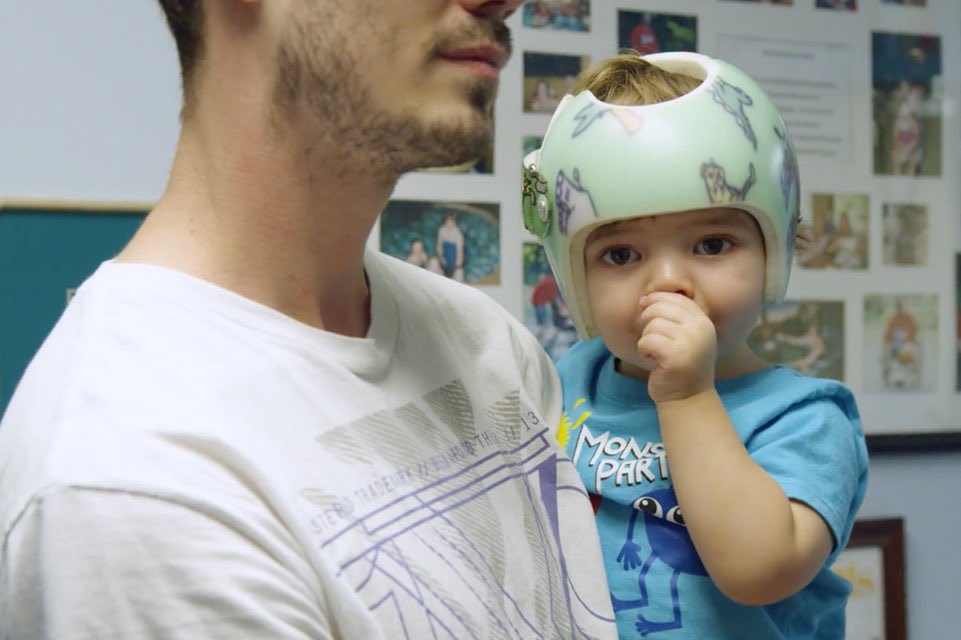 Padre sosteniendo al hijo que está usando su protector craneal