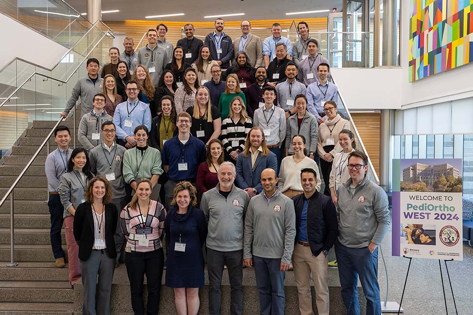 Grand groupe de participants à la conférence, panneau de bienvenue du Pediortho West 2024