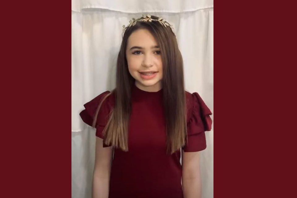 Maddie standing in front of curtain in red dress with wreath on her head