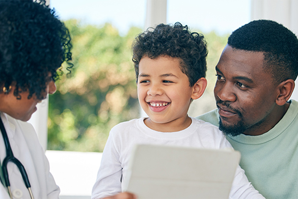 Doctor holding tablet and speaking with male patient and his father