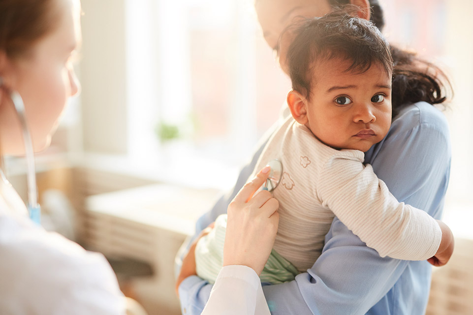 mother holds baby while physician examines him