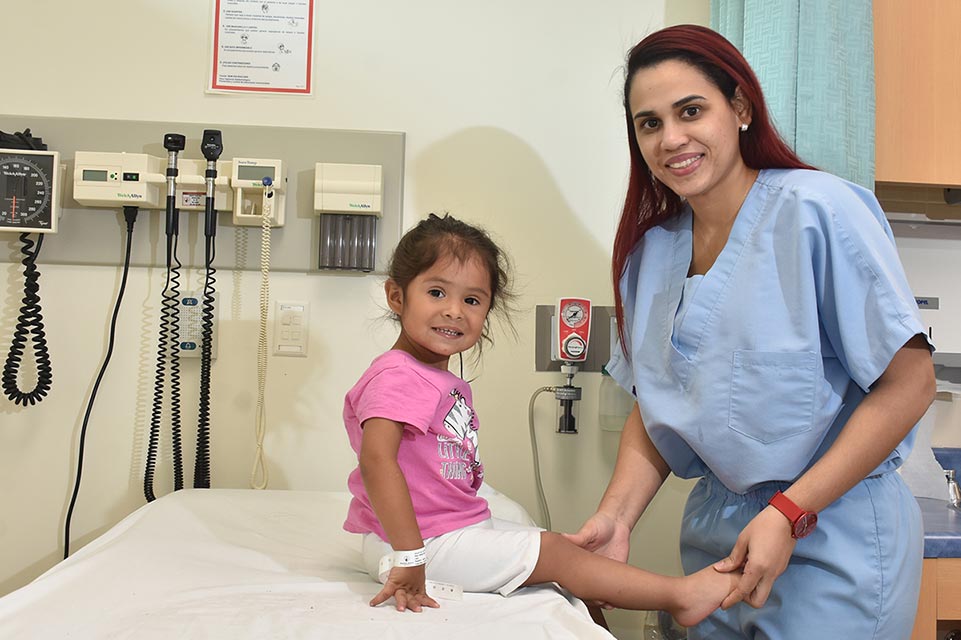 Doctora sosteniendo pierna de paciente con un <i>short</i> color blanco y una blusa color rosa