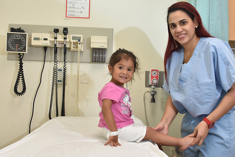 Doctora sosteniendo pierna de paciente de short color blanco y blusa color rosa