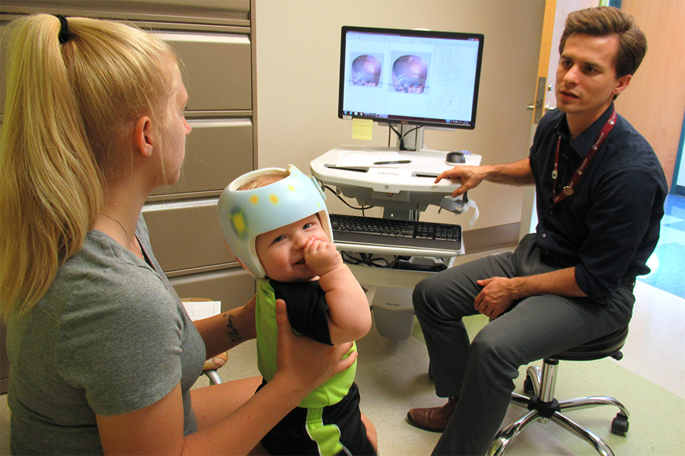 mom holding baby wearing helmet, physician