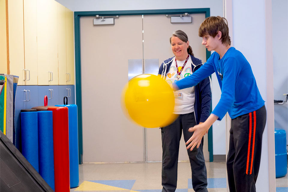 Patient bounces ball with physical therapist