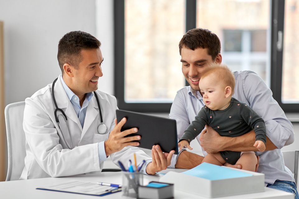 baby sits on dad's lap speaking with physician