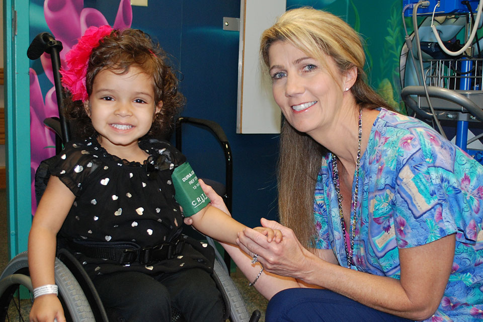 Nurse kneeling next to smiling girl in wheelchair