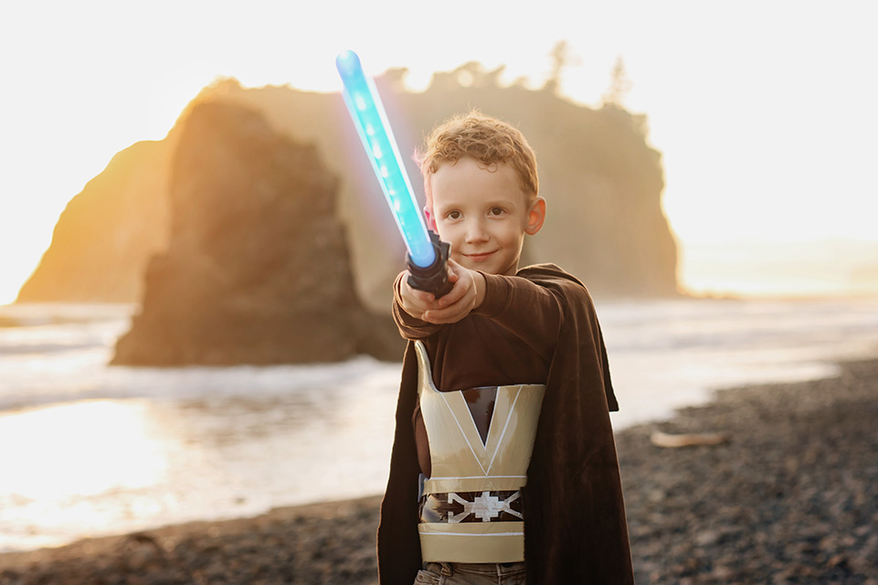 Niño parado en una playa disfrazado sosteniendo una espada de plástico con luz